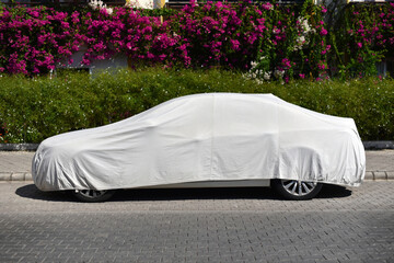 a parked car covered with a sun protection fabric on the street of green city