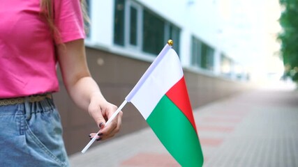 Unrecognizable woman holding Malagasy flag. Girl walking down street with national flag of Madagascar