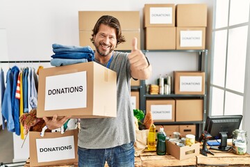 Handsome middle age man holding donations box for charity at volunteer stand approving doing positive gesture with hand, thumbs up smiling and happy for success. winner gesture.