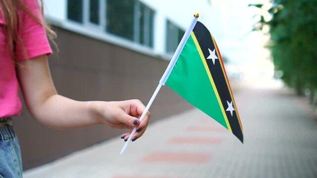 Unrecognizable woman holding Kittitian or Nevisian flag. Girl walking down street with national flag of Saint Kitts and Nevis