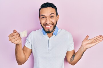 Hispanic man with beard holding white protein powder celebrating achievement with happy smile and winner expression with raised hand