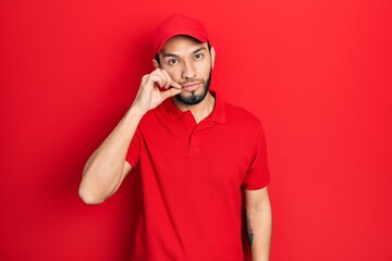 Hispanic man with beard wearing delivery uniform and cap mouth and lips shut as zip with fingers....