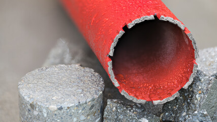 Red water cooled diamond core drill bit on round bored piece of gray concrete tile. Closeup of...