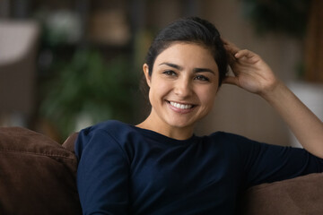 Smiling young mixed race female relax on couch in living room look in distance dreaming...