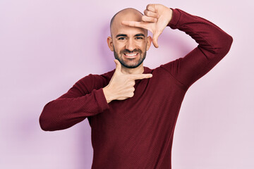 Fototapeta premium Young bald man wearing casual clothes smiling making frame with hands and fingers with happy face. creativity and photography concept.