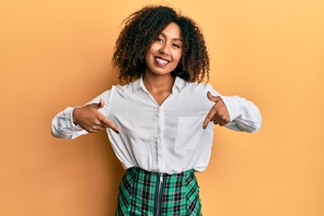 Beautiful african american woman with afro hair wearing scholar skirt looking confident with smile on face, pointing oneself with fingers proud and happy.