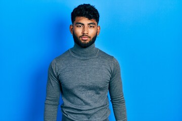 Arab man with beard wearing turtleneck sweater relaxed with serious expression on face. simple and...