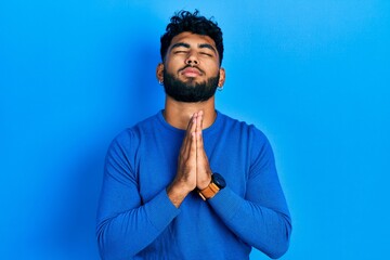 Arab man with beard wearing casual blue sweater begging and praying with hands together with hope expression on face very emotional and worried. begging.