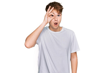 Young caucasian man wearing casual white t shirt doing ok gesture shocked with surprised face, eye looking through fingers. unbelieving expression.