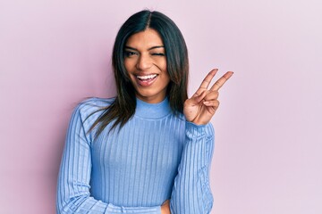 Young latin transsexual transgender woman wearing casual clothes smiling with happy face winking at the camera doing victory sign. number two.