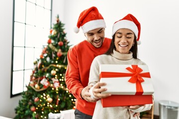 Fototapeta na wymiar Young latin couple smiling happy and hugging unboxing christmas gift at home.