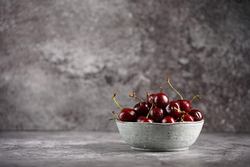 Fresh sweet and sour dark red cherries in a grey scandi bowl on grey background