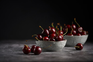 Fresh sweet and sour dark red cherries in two grey scandi bowls on black background