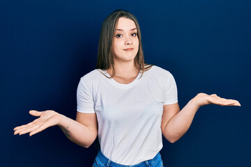 Young hispanic girl wearing casual white t shirt clueless and confused expression with arms and hands raised. doubt concept.