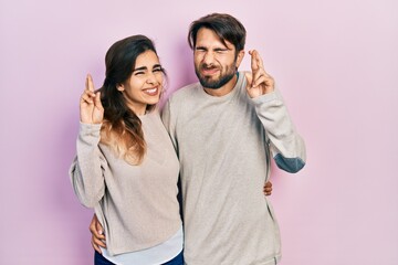 Naklejka premium Young hispanic couple wearing casual clothes gesturing finger crossed smiling with hope and eyes closed. luck and superstitious concept.