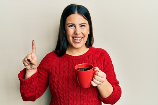 Beautiful brunette woman drinking a cup of black coffee smiling with an idea or question pointing finger with happy face, number one - Powered by Adobe