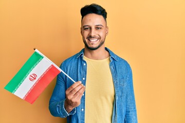 Young arab man holding iran flag looking positive and happy standing and smiling with a confident smile showing teeth