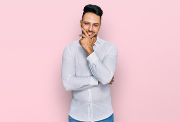 Young arab man wearing casual clothes looking confident at the camera smiling with crossed arms and hand raised on chin. thinking positive.