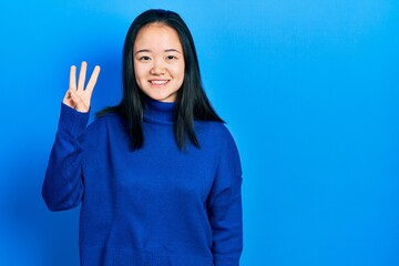 Young chinese girl wearing casual clothes showing and pointing up with fingers number three while smiling confident and happy.