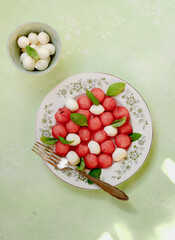Watermelon salad with mozzarella cheese and fresh basil leaves on green background. Caprese salad with watermelon balls. Top view flat lay.