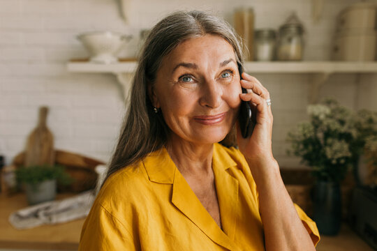 Cheerful Middle-aged Female Communicating With Friends Or Relatives On Smartphone. Attractive Smiling Woman Talking On Cellphone And Looking Away With Happiness