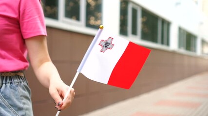 Unrecognizable woman holding Maltese flag. Girl walking down street with national flag of Malta