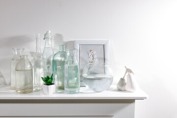 A set of water bottles of different shapes with a photo frame and a pot with artificial succulent is on the dresser