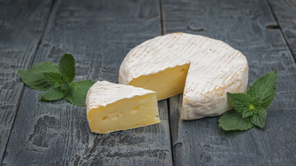 Camembert cheese with a cut piece and mint leaves on a black wooden table.