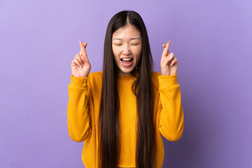 Young Chinese girl over isolated purple background with fingers crossing