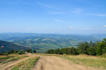 Summer mountain landscape with ski lift on the green grassy hill, and  the valley with Pylypets...
