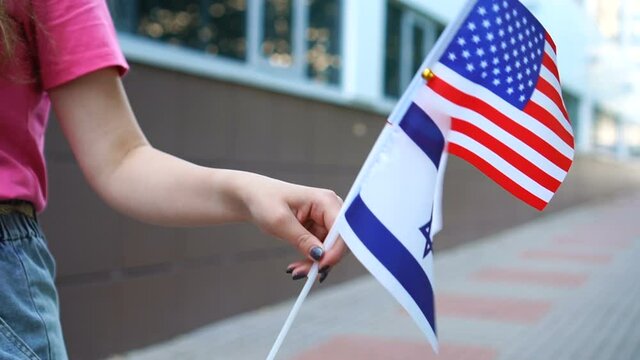 Unrecognizable woman holding American and Israeli flags. Girl walking down street with national flags of USA and Israel