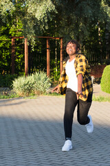 a happy African American woman in the park makes a jump in the summer