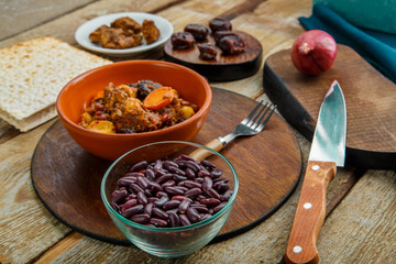 Jewish dish chelnt with meat in a plate on a wooden table on a stand next to a knife and ingredients.