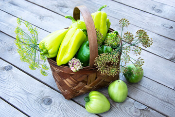 Vegetables in the basket. A wicker basket with peppers, tomatoes and dill stands on a wooden background.