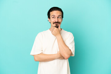 Young caucasian man isolated on blue background thinking an idea while looking up