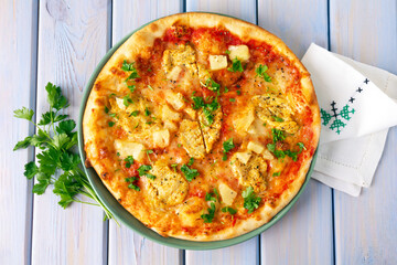 Pizza with chicken, pineapple and mozzarella on wooden table.