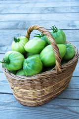 Vegetables in a basket close-up. A wicker basket with green tomatoes stands on a wooden background. Vertical background.