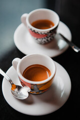 Traditional Italian coffee. Two small colorful espresso cups on a white saucer with a spoon on a black table at the bar in Milan, Lombardy, Italy. European beverages and drinks. 