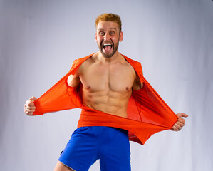 a muscular man in blue shorts rips his red T-shirt and screams with his mouth wide open. Gray...