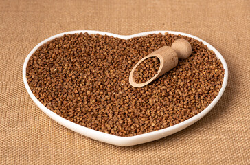Dry buckwheat on a white plate in the shape of a heart. On a white brown burlap.