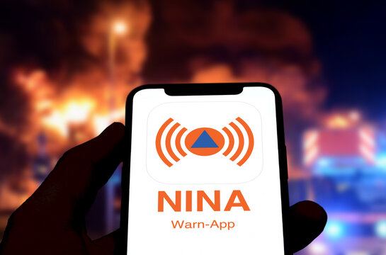 Smartphone zeigt NINA Warn-App, im Hintergrund die Szenerie eines Gro&szlig;brands in der Nacht, Notfall-Informations- und Nachrichten-App, Bundesamt f&uuml;r Bev&ouml;lkerungsschutz und Katastrophenhilfe, Warnmelder