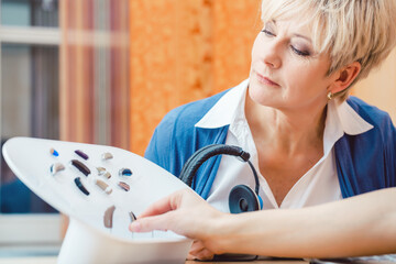 Senior woman with impairment choosing hearing aid in shop - 445931846