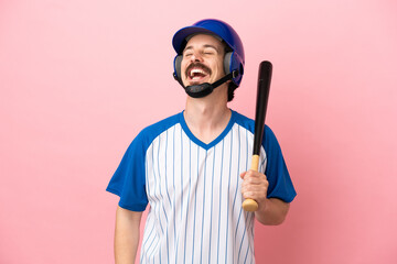 Young caucasian man playing baseball isolated on pink background laughing