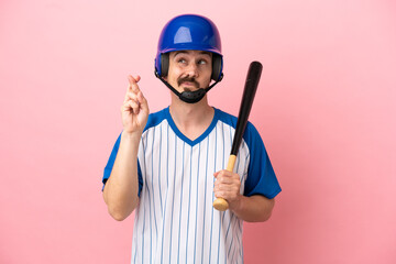 Young caucasian man playing baseball isolated on pink background with fingers crossing and wishing the best