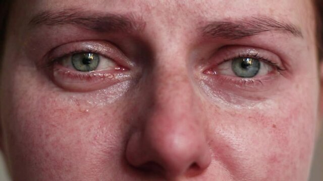 Worried young woman is crying. Upset depressed girl with colorful eyes and tears on cheeks alone at home. Tears are flowing.