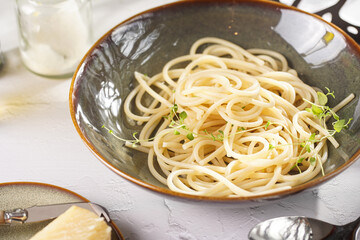 Italian spaghetti with parmesan cheese and fresh thyme in dark green bowl on white concrete surface, with olive oil and balsamic vinegar in the back