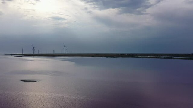 A wind farm on the shores of a pink lake. Evening time. Aerial view. Lake Lemuria (Pink Lake) is a lake in the Kherson region of Ukraine