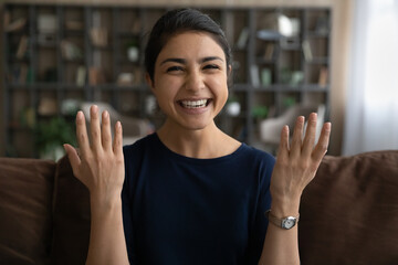 Close up headshot portrait of smiling young Indian woman talk speak on video call sit on couch at home. Happy millennial mixed race female coach trainer have webcam digital virtual event on gadget.