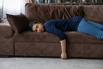 Exhausted millennial Indian woman lying on sofa in living room sleep or take nap after hard day....