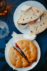 Traditional Italian food. Crispy panini and piadina sandwiches with prosciutto (speck), cheese, lettuce and vegetables with fresh drinks on a table with a blue tablecloth. Healthy European snack.